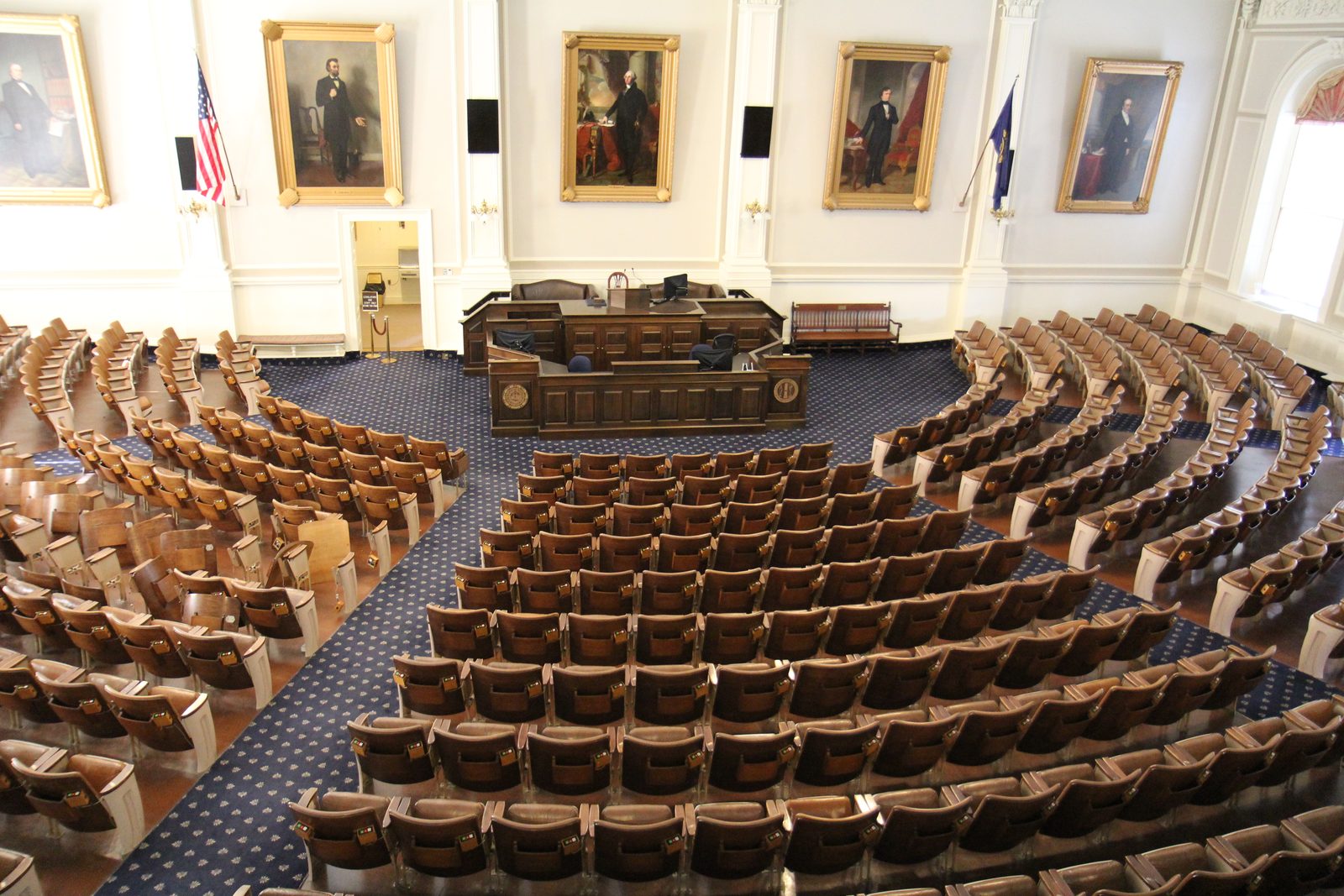 Rows of wooden seats in the New Hampshire House of Representatives chamber at the State House in Concord, seen from the balcony